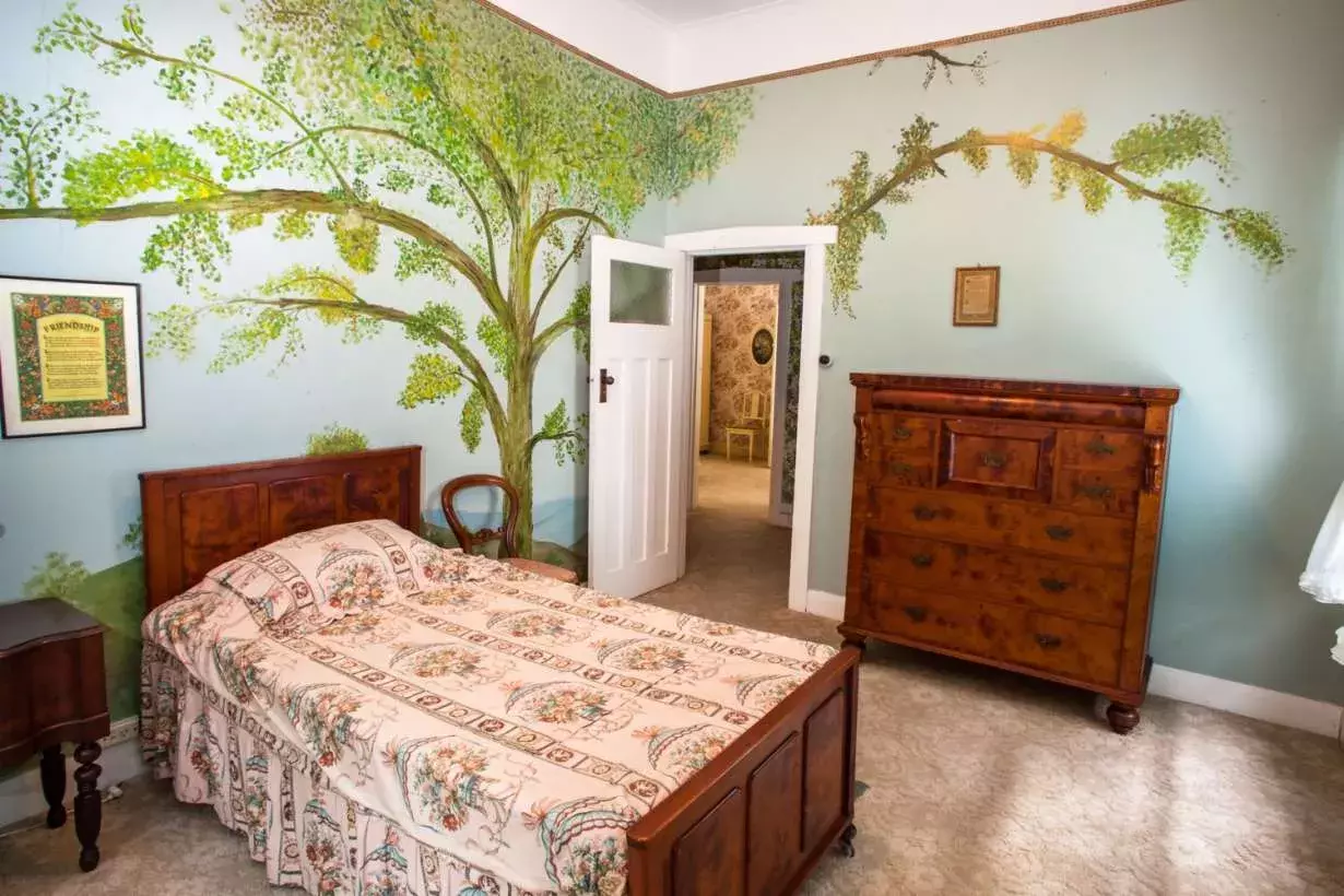 The bedroom at Home Hill a wooden chest, a timber bedhead and wallpaper featuring a large tree that covers the whole wall.  