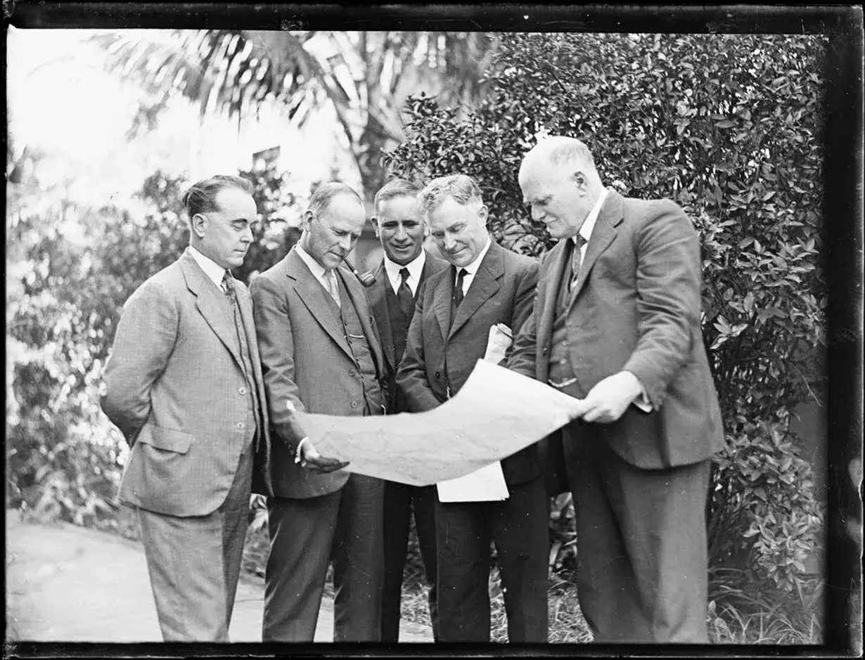 Dr Earle Page examining a plan with four other men 
