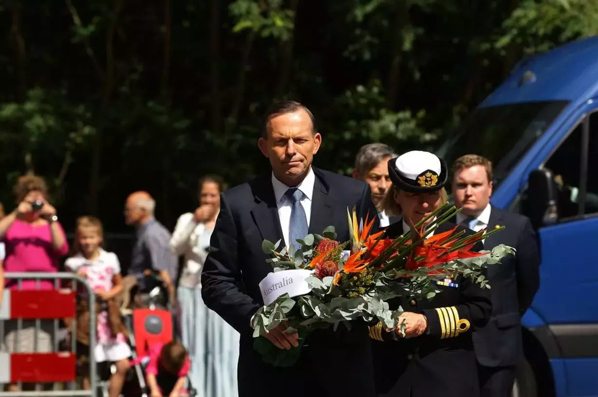 Tony Abbott carries flowers at a memorial. 
