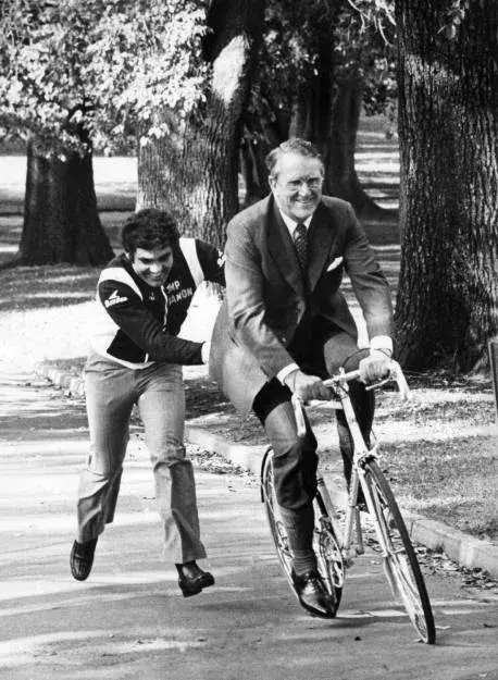 Malcolm Fraser rides a bike while being pushed by somebody.  