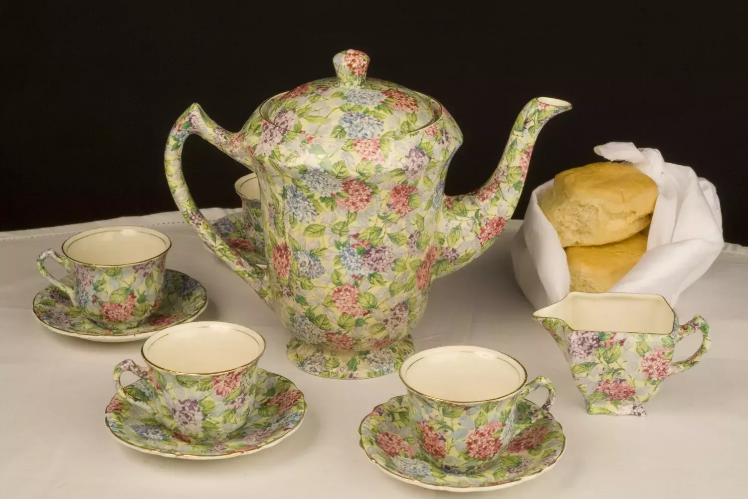 A teapot and three tea cups and a pourer decorated in ornate flower pattern. 