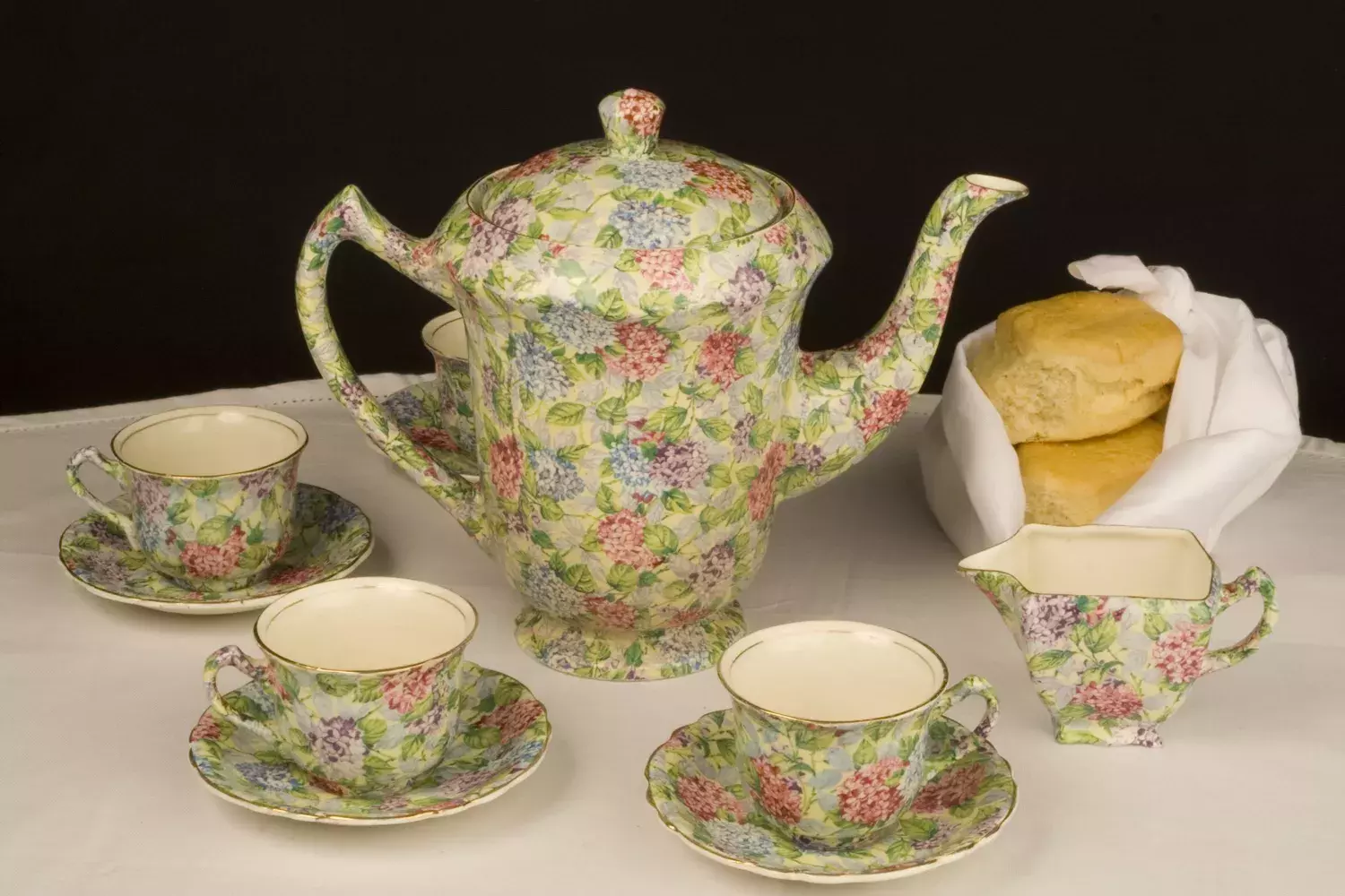 A teapot and three tea cups and a pourer decorated in ornate flower pattern.