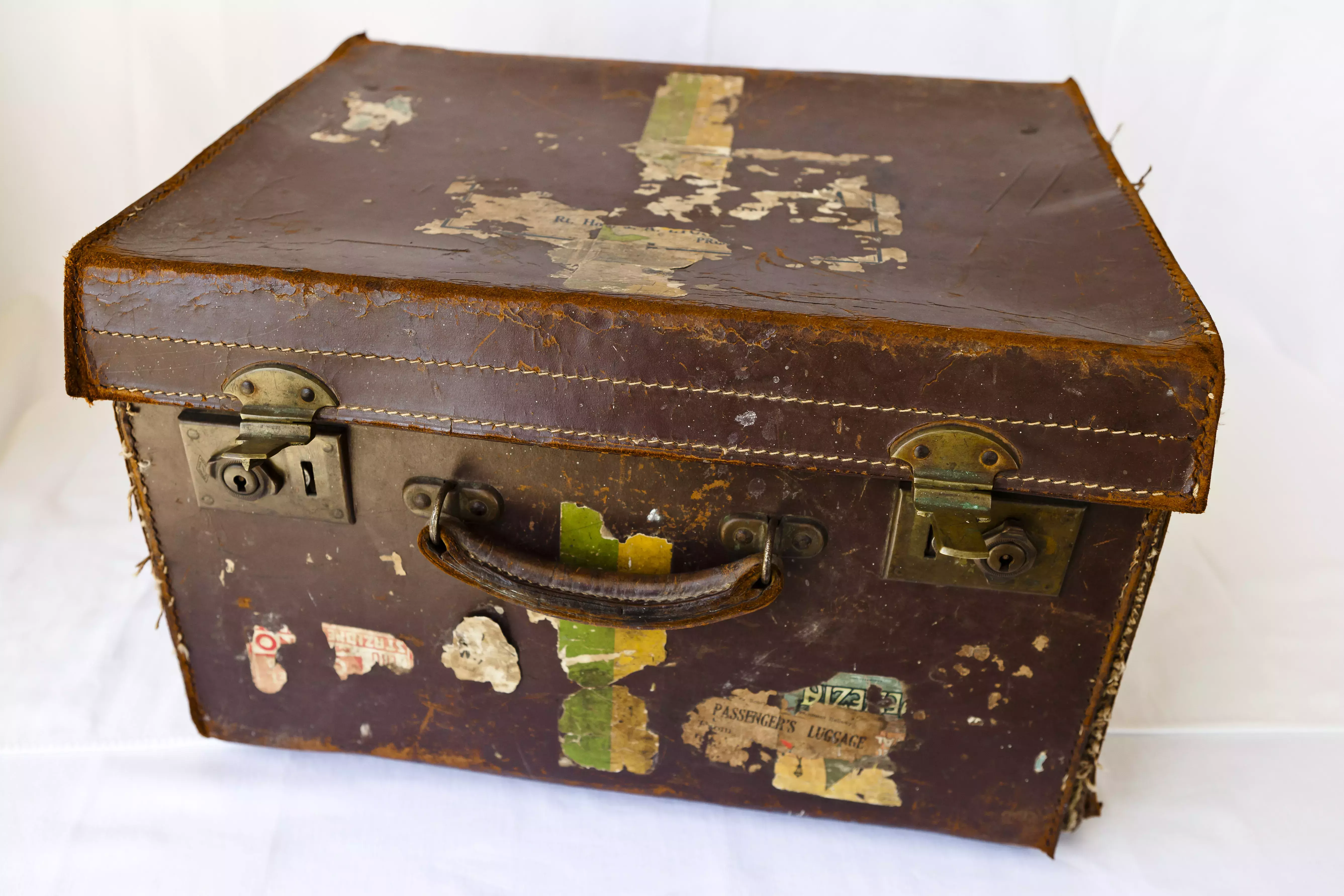 A brown tattered square suitcase with peeling stickers.
